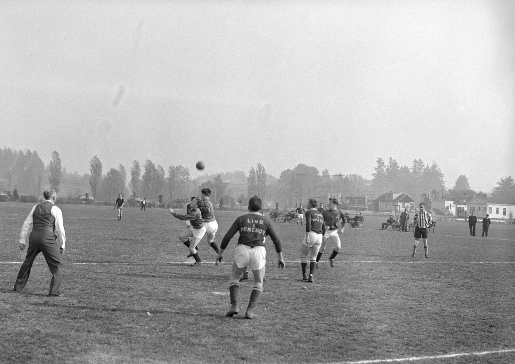 Players for the Albina Engine & Machine Works soccer team, the Subchasers, on a field during a game against a team for Lind & Pomeroy. The ball can be seen in the air, with blurry players underneath